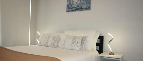 A bedroom with a bed, pillows, a nightstand, a painting on the wall, and a window.