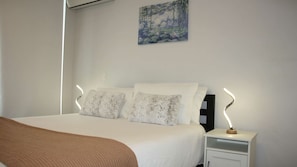 Ein Schlafzimmer mit einem Bett, Kissen, einem Nachttisch, einem Bild an der Wand und einem Fenster.