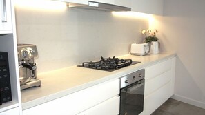 Une cuisine moderne équipée d’une machine à expresso intégrée, d’une cuisinière à gaz, d’un grille-pain et d’un lave-vaisselle.
