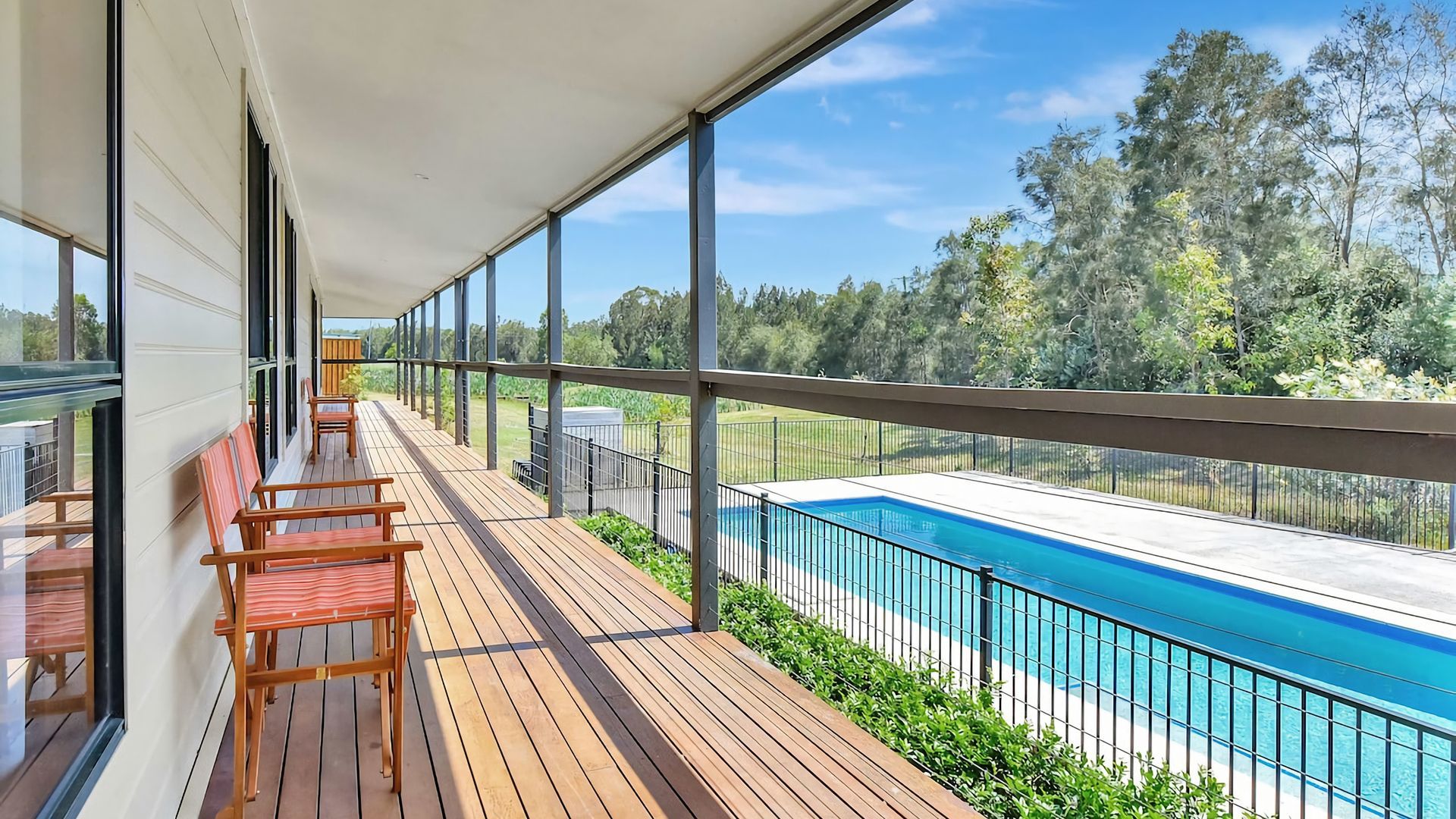 A balcony with a pool, wooden deck, and chairs.