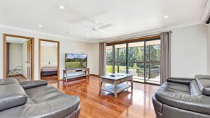 A spacious living room with a flat-screen TV, leather sofas, a wooden coffee table, and large glass doors leading to an outdoor area. - Casa Sangiovese | In the Heart of the Hunter Valley (Pokolbin)
