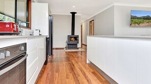 A modern kitchen with a wood-burning stove, white cabinetry, and a wooden floor. - Casa Sangiovese | In the Heart of the Hunter Valley (Pokolbin)