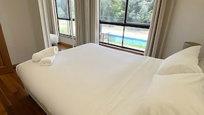 A hotel room with a large bed, a window with a view of a blue fence and greenery, and a wooden floor. - Casa Sangiovese | In the Heart of the Hunter Valley (Pokolbin)