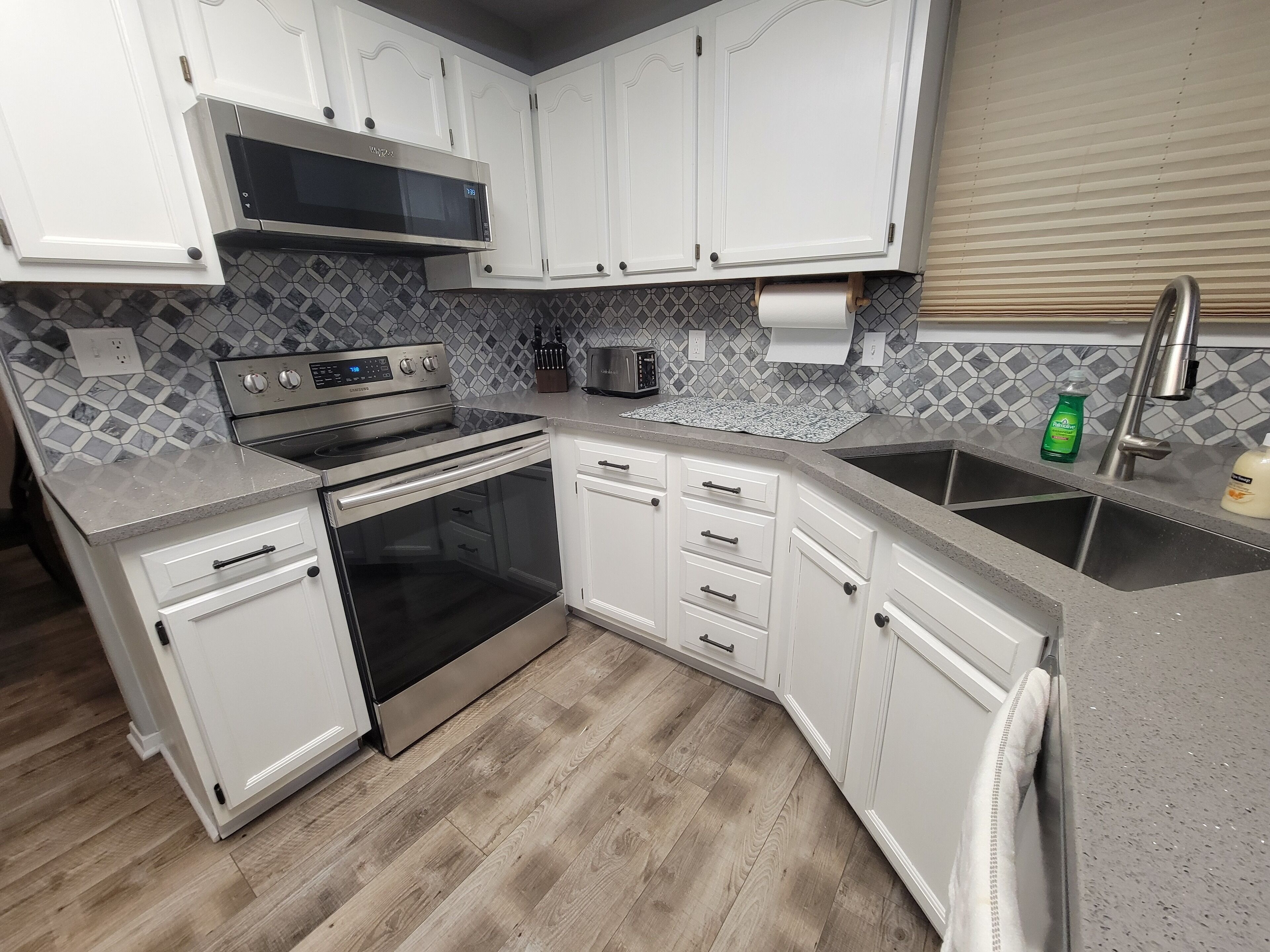A modern kitchen with white cabinets, a stainless steel stove, a microwave, and a sink.