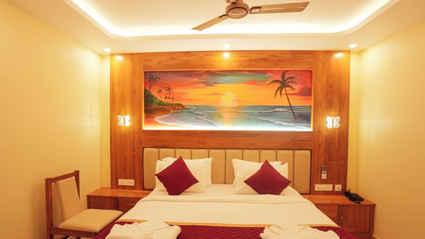 A hotel room with a bed, a chair, a painting of a sunset, and a ceiling fan. - Le Kumar Residency (Puducherry)