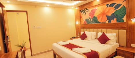 A hotel room with a bed, bedside tables, a desk with a chair, a ceiling fan, and a wall with a floral mural.