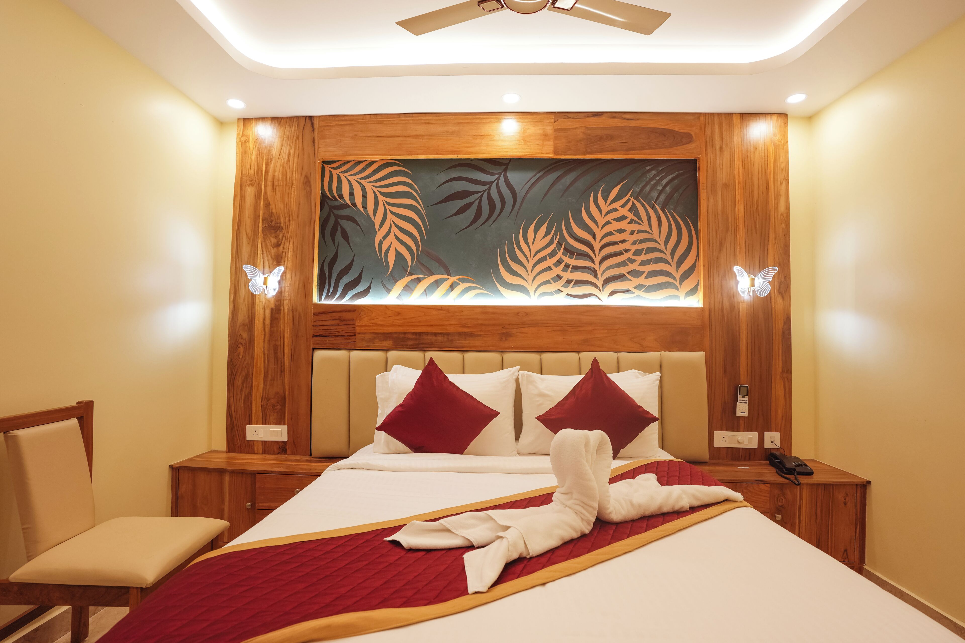 Quarto de hotel com cama, cadeira, mesa de cabeceira e parede com desenhos de folhas.