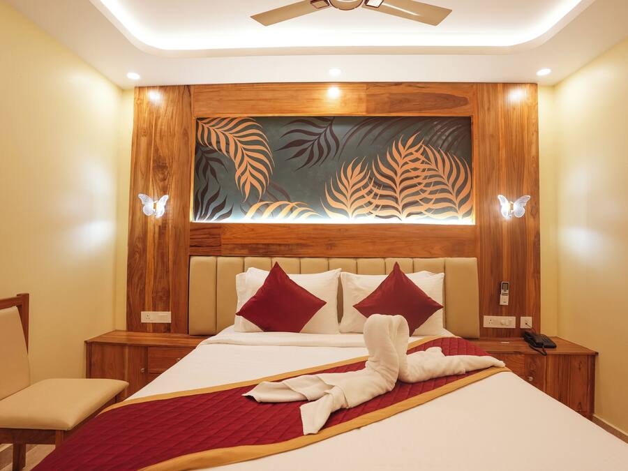 Quarto de hotel com cama, cadeira, mesa de cabeceira e parede com desenhos de folhas.