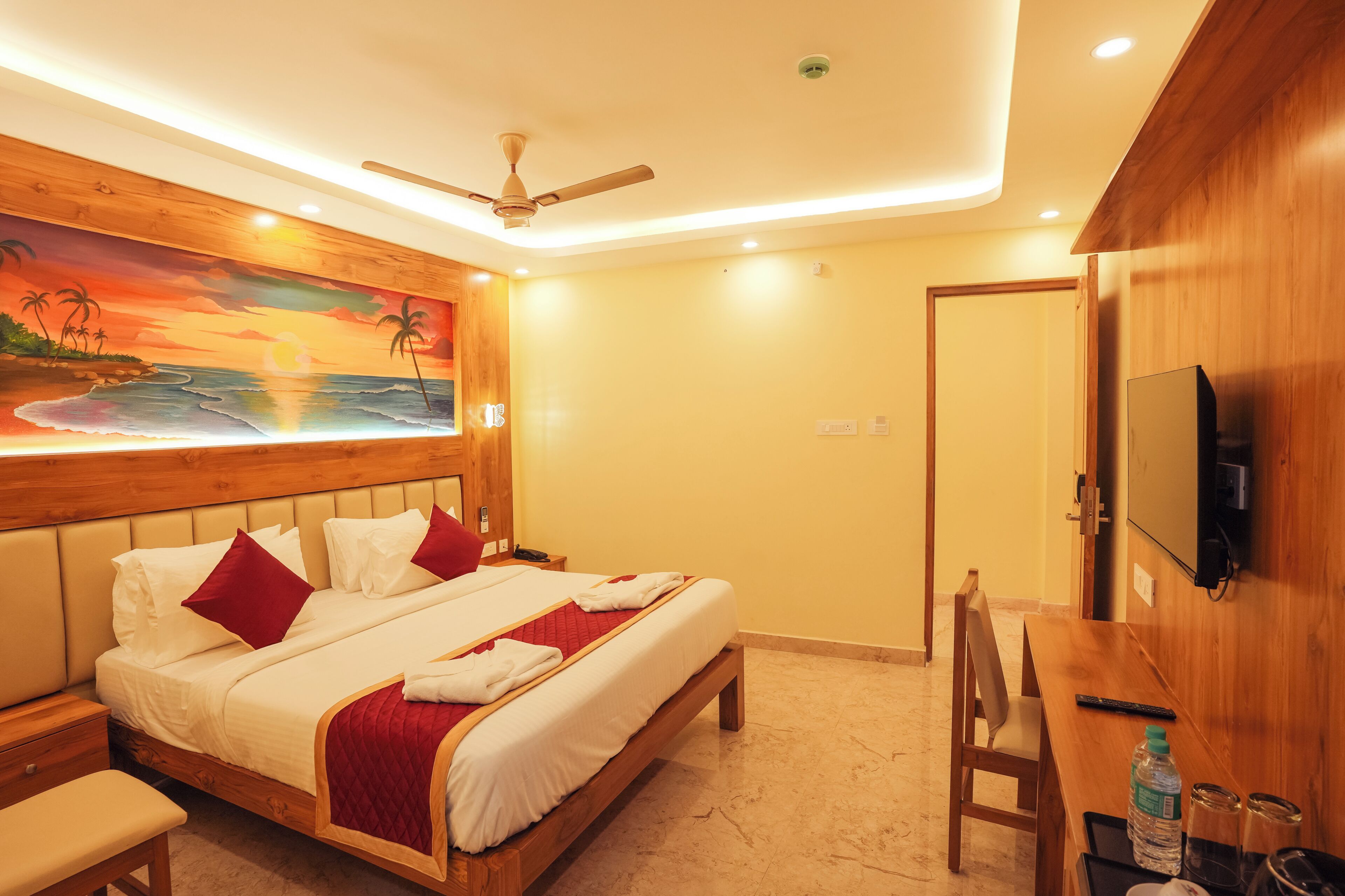 A hotel room with a bed, a desk, a chair, a TV, and a painting on the wall.