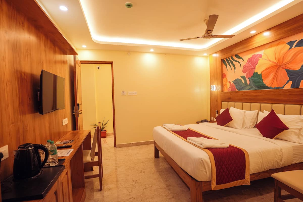 A hotel room with a bed, a desk with a kettle, a TV, and a ceiling fan.