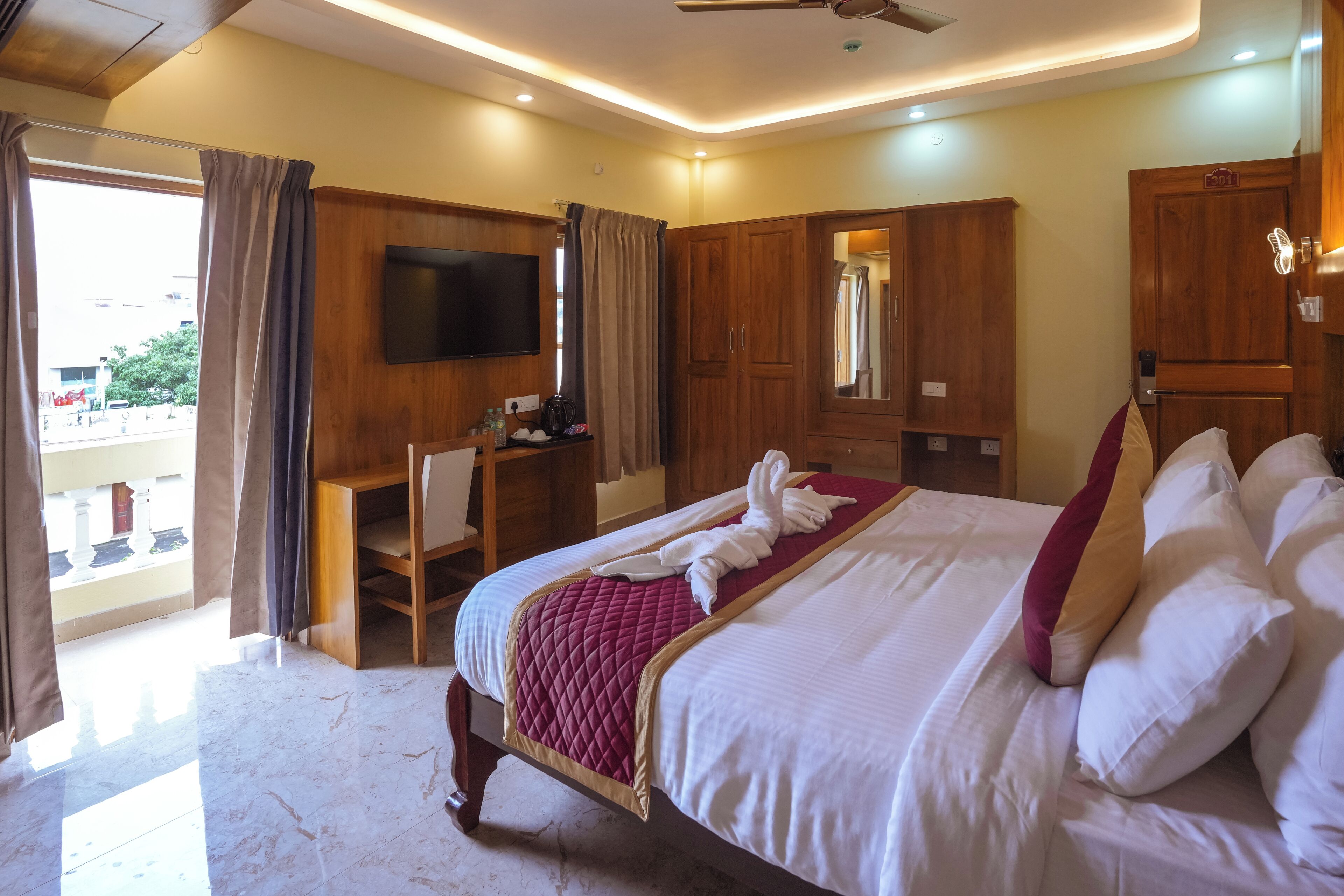 A hotel room with a bed, a desk, a TV, and a balcony view.