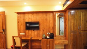 A wooden room with a TV mounted on the wall, a desk with a chair, and a cabinet. - Le Kumar Residency (Puducherry)