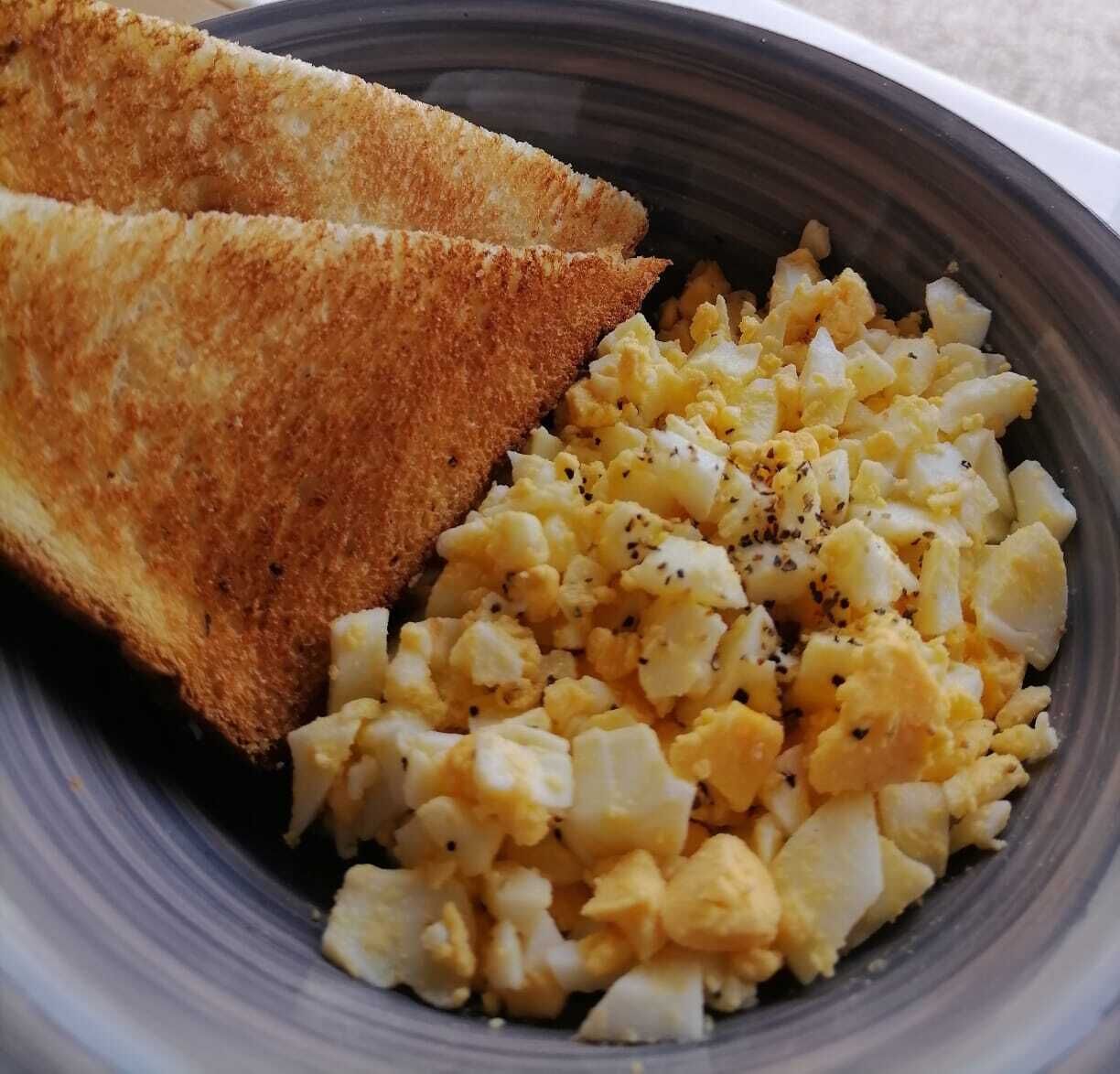 A bowl containing scrambled eggs and toasted bread.