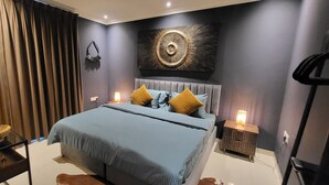 Een moderne slaapkamer met een groot bed, een hoofdbord, een kunstwerk aan de muur en een nachtkastje met een lamp.