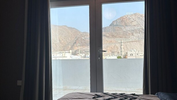 Hotelkamer met een groot bed en uitzicht op een stadsbeeld en bergen door een schuifdeur.