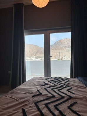 Hotelkamer met een groot bed en uitzicht op een stadsbeeld en bergen door een schuifdeur.