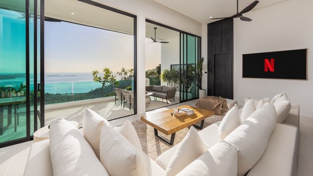 A modern living room with a white sofa, a wooden coffee table, and a large window offering a view of the ocean. - SOMA 4 Bedrooms SEAVIEW Pool Villa (Koh Samui)