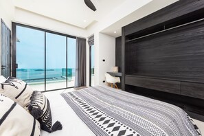 A modern bedroom with a large bed, a view of the sea through floor-to-ceiling windows, and a dark wood panel wall. - SOMA 4 Bedrooms SEAVIEW Pool Villa (Koh Samui)
