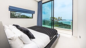 A modern bedroom with a large bed, a view of the sea, and a window with a blue curtain. - SOMA 4 Bedrooms SEAVIEW Pool Villa (Koh Samui)
