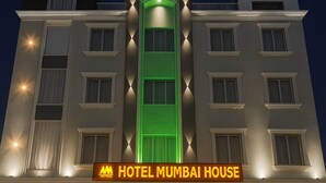 A hotel with a prominent green vertical feature, a sign reading "HOTEL MUMBAI HOUSE," and a car parked in front. - Hotel Mumbai House - Pithampur (Pithampur)