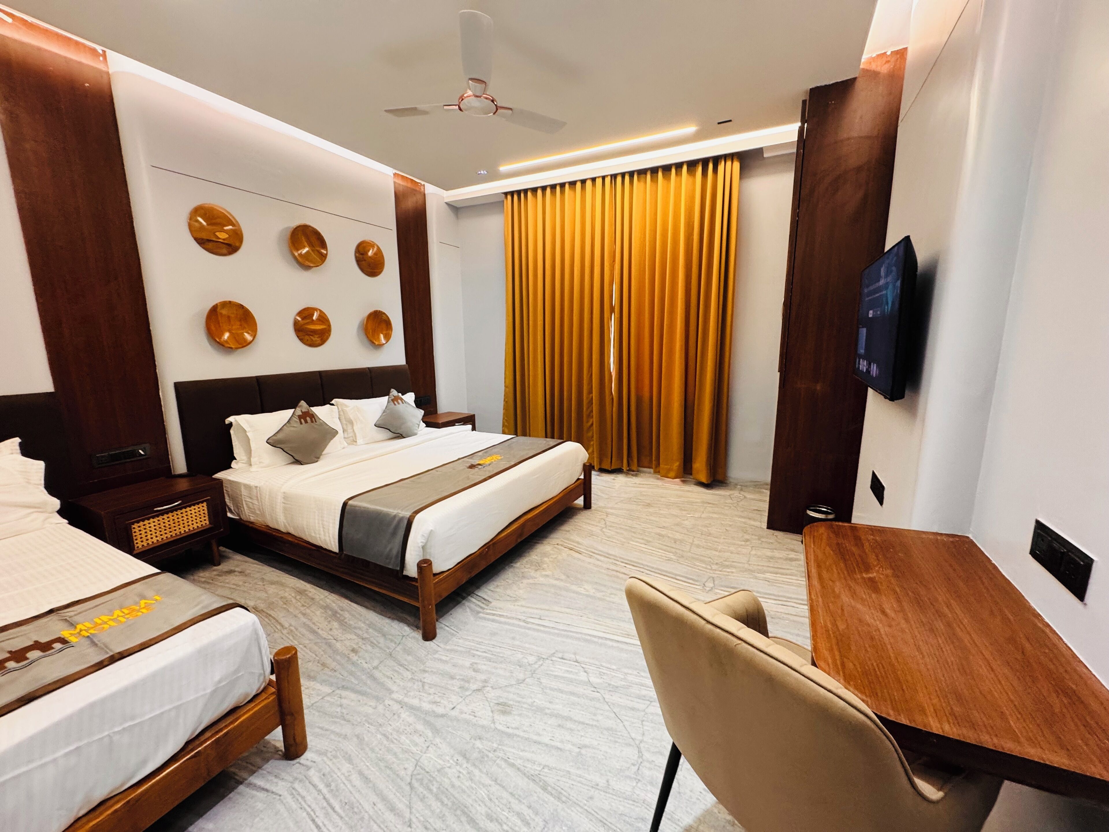 A hotel room with a large bed, a desk, a chair, a television, and a ceiling fan.