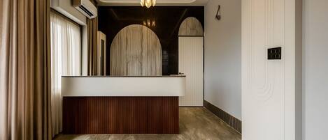 A modern reception area with a wooden reception desk, a chandelier, and a large arched window.