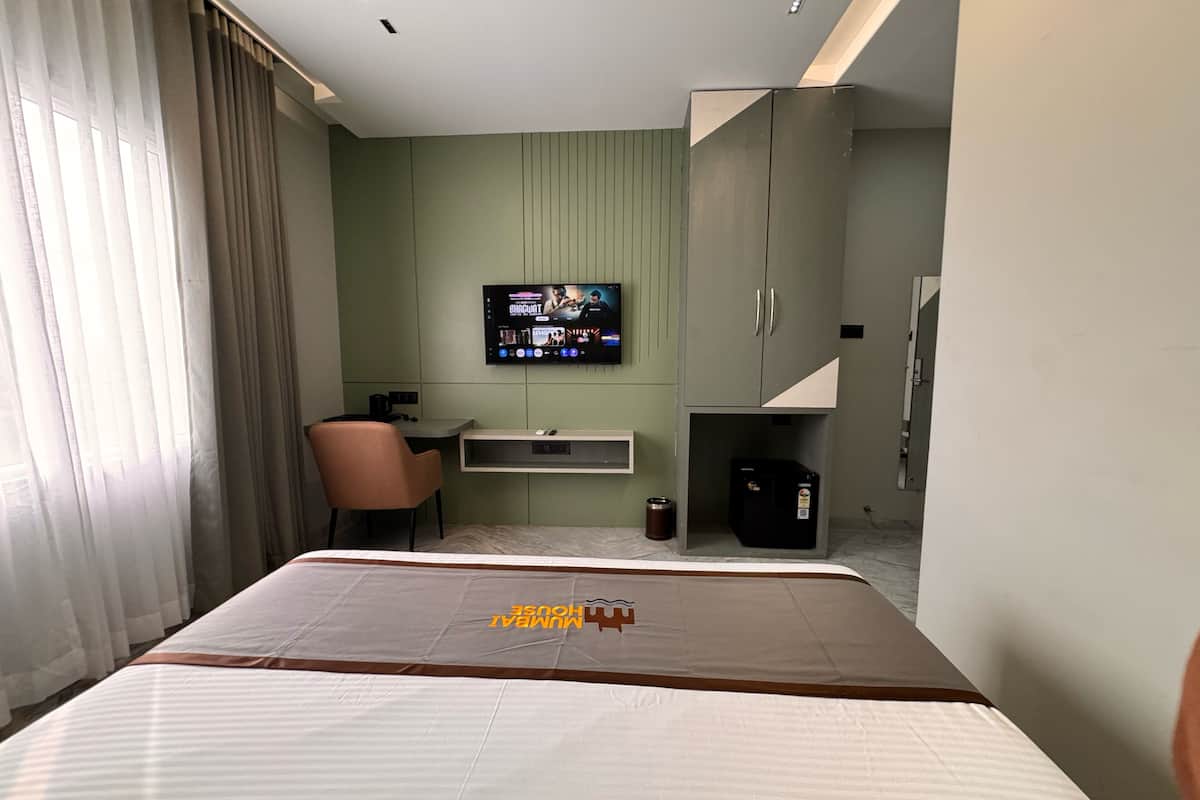 Una habitación de hotel con cama, escritorio, silla, televisor y armario.