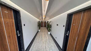 A hallway with wooden doors, potted plants, and a marble floor. - Hotel Mumbai House - Pithampur (Pithampur)