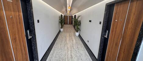 A hallway with wooden doors, potted plants, and a marble floor.