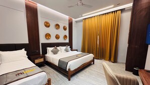 A hotel room with two beds, a wooden headboard, a ceiling fan, a large window with yellow curtains, and a wall-mounted clock. - Hotel Mumbai House - Pithampur (Pithampur)