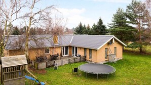 Ein Haus mit einem umzäunten Garten, einem Trampolin und einem Spielhaus.