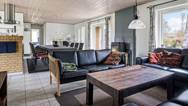 Ein modernes Wohnzimmer mit Kamin, Ledersofas, einem Essbereich und einer durch eine offene Tür sichtbaren Küche.