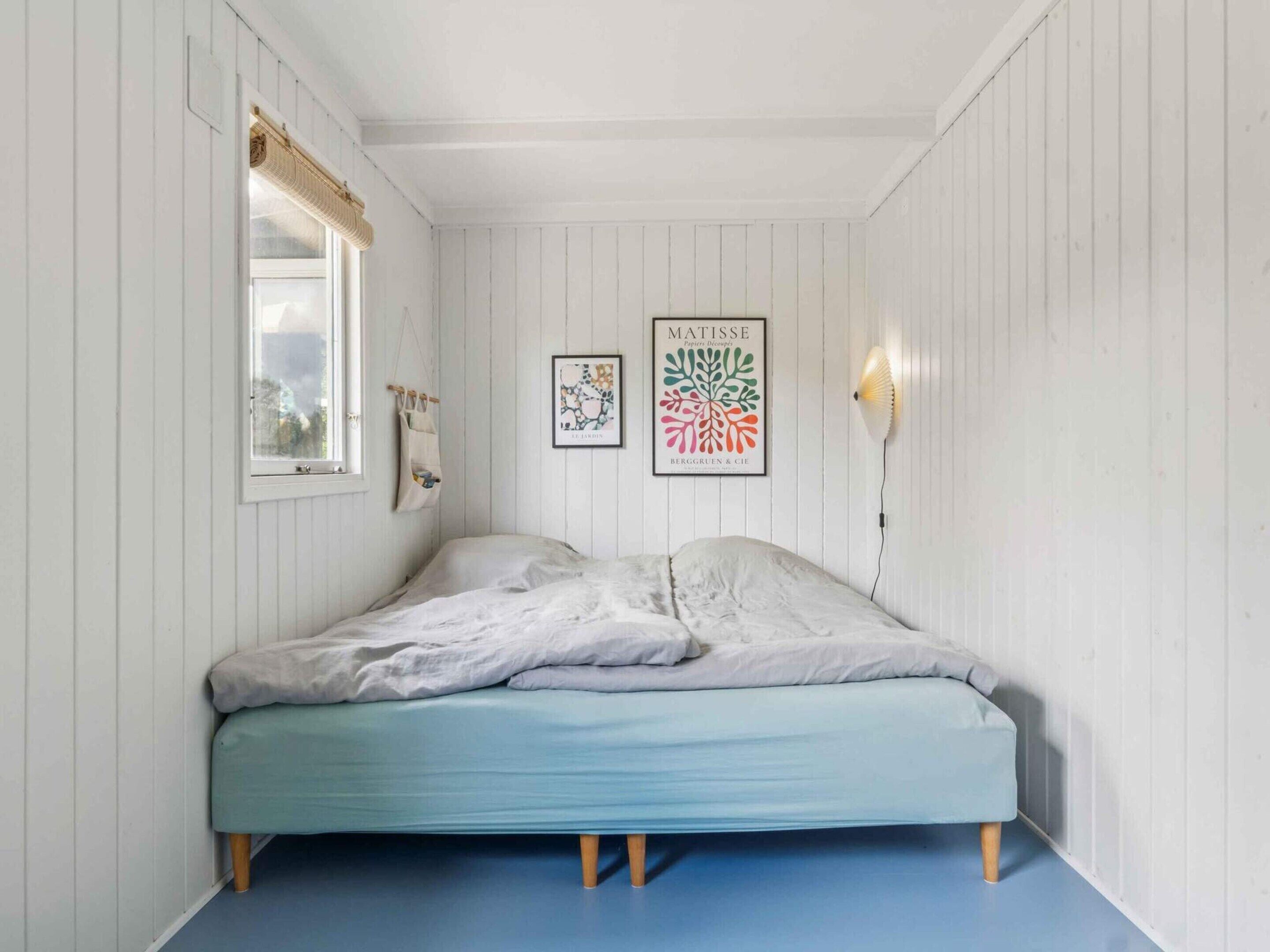 A bedroom with a bed, a window, and two wall-mounted artworks.