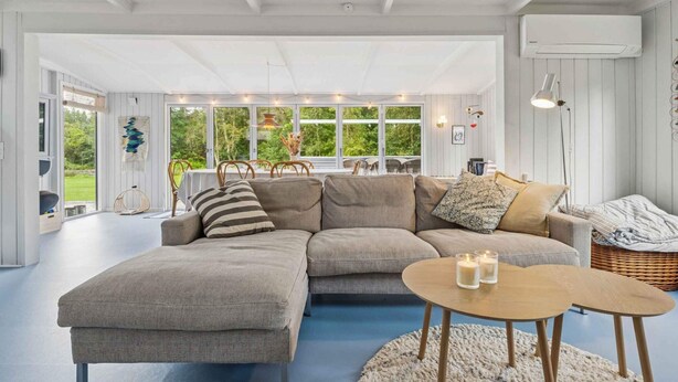 A modern living room with a sectional sofa, a round coffee table, and a view of greenery through large windows. - 4 Star Holiday Home in Hojslev (Hojslev)