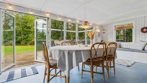 A dining area with a round table, wicker chairs, and a view of the outdoors through large glass doors. - 4 Star Holiday Home in Hojslev (Hojslev)