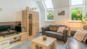 A modern living room with a flat-screen TV, wooden cabinet, leather sofa, and a small wooden table. - Tastefully and Modernly Furnished 5-person Bungalow (De Waal)