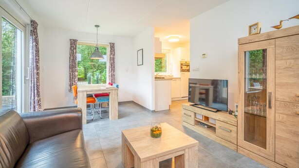 A modern living room with a sofa, a coffee table, a TV, and a kitchen area in the background. - Tastefully and Modernly Furnished 5-person Bungalow (De Waal)