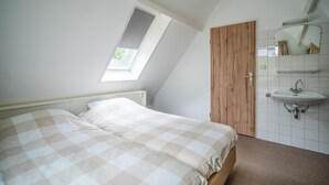 A bedroom with a bed, a skylight, a wooden door, and a wall-mounted sink. - Tastefully and Modernly Furnished 5-person Bungalow (De Waal)