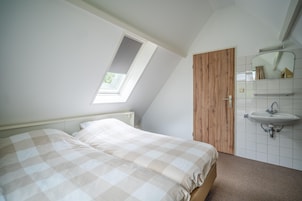 Quarto com cama, claraboia, porta de madeira e pia fixada na parede.