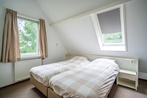 A bedroom with two beds, a window with curtains, a radiator, and a small bedside table. - Tastefully and Modernly Furnished 5-person Bungalow (De Waal)