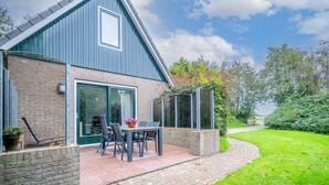 A modern house with a brick exterior and a blue roof, featuring a patio with a table and chairs, and a well-maintained garden. - Tastefully and Modernly Furnished 5-person Bungalow (De Waal)