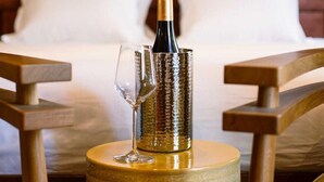 A bottle of wine on a wooden table with a glass, in a room with a bed and pillows in the background. - Confidential Room 3, a Stone's Throw From the Louvre (Paris)