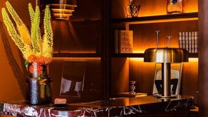 A well-lit reception area with a marble counter, a vase of flowers, a lamp, and a shelf with books and a glass bottle. - Confidential Room 3, a Stone's Throw From the Louvre (Paris)
