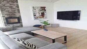 Un salon moderne avec un canapé gris, une table basse en bois, un téléviseur à écran plat, une cheminée et un grand tableau abstrait.
