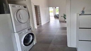 Un espace buanderie équipé d’un lave-linge et d’un sèche-linge, un couloir menant à une autre pièce et un placard blanc.