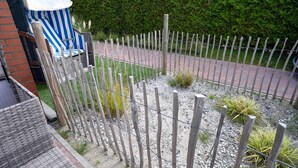 A fenced outdoor area with a gravel path, a blue and white striped chair, and a brick wall. - Moderne Ferienwohnung in Ruhiger Lage, Bensersiel (Esens)