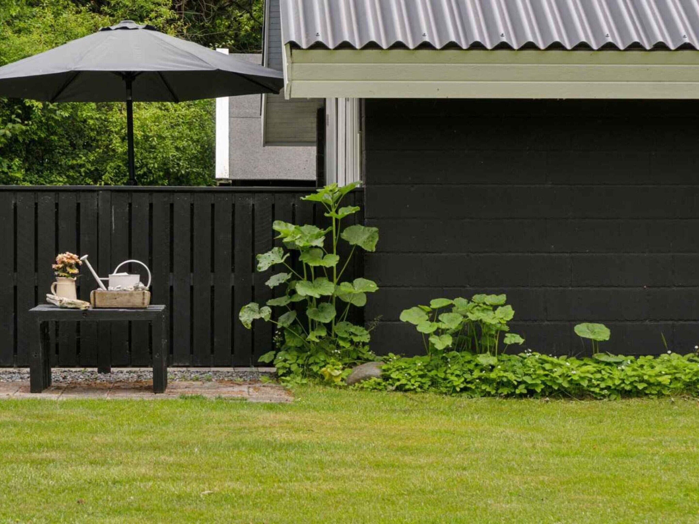 A black wooden fence, a black bench with a white pitcher and flowers, and a large umbrella.