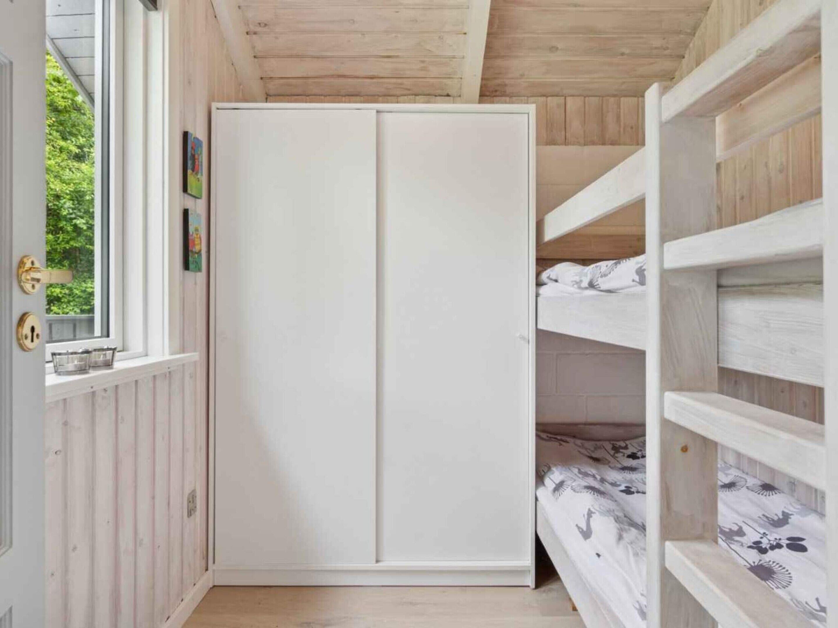 Ein Zimmer mit Holzbalkendecke, einem weißen Kleiderschrank und einem Etagenbett mit gemusterten Betttextilien.