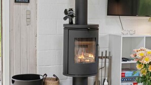 A modern living room with a black wood-burning stove, a television mounted on the wall, and a bookshelf with books and decorative items. - 4 Star Holiday Home in Hurup Thy (Hurup Thy)