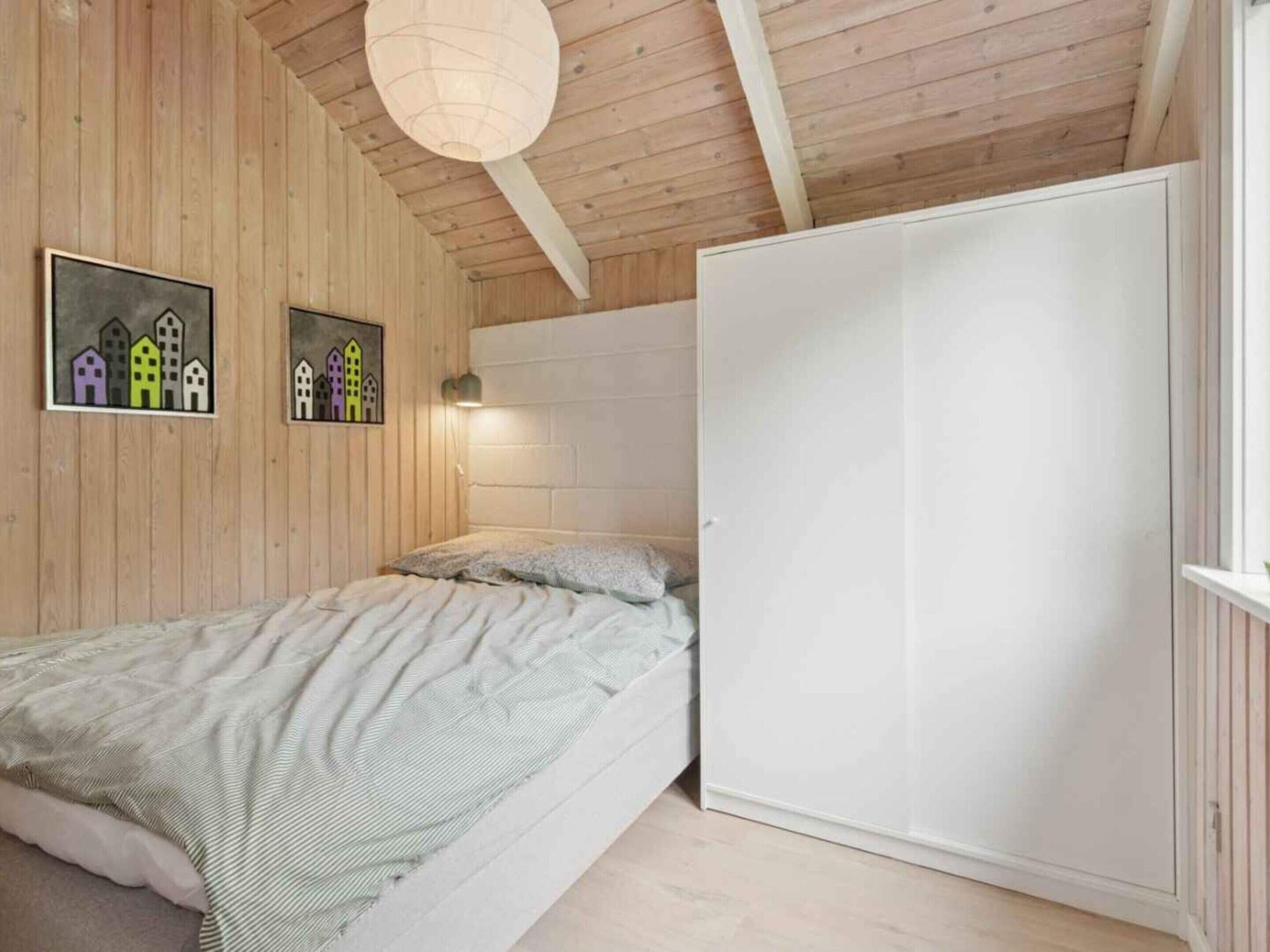 Une chambre à coucher comprenant un lit, une armoire, des murs en bois et deux appliques murales.